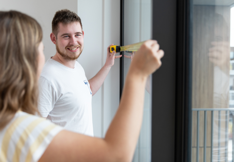 Two people measuring window of a room